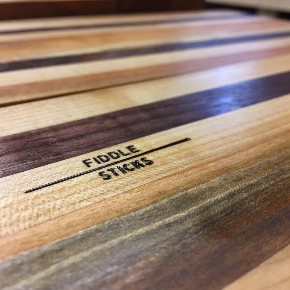 Close-up of a striped hardwood cutting board engraved with the FiddleSticks logo