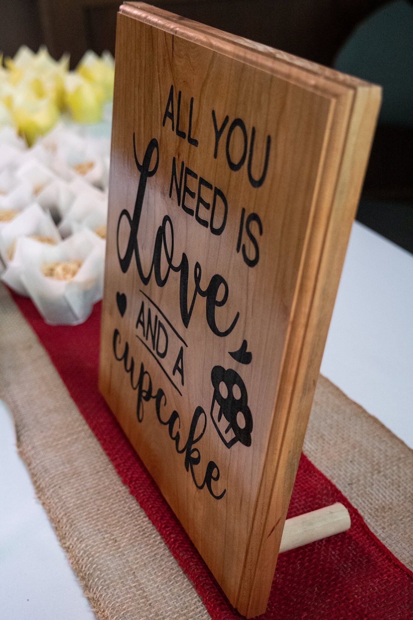 Cherry wood sign reading 'All you need is love and a cupcake' on a dessert table