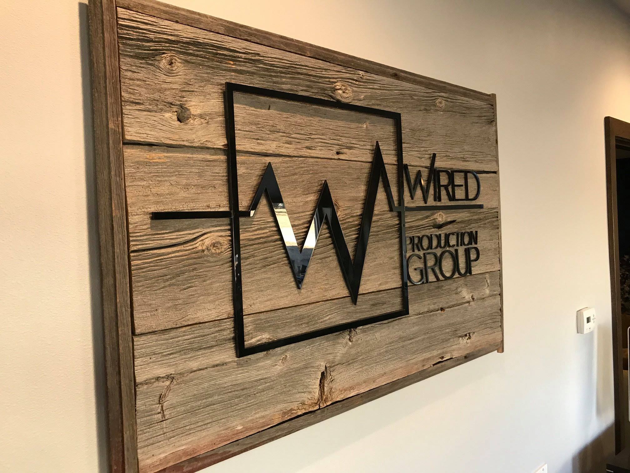Reclaimed barnwood sign with a raised black acrylic Wired Production Group logo, hung in an office